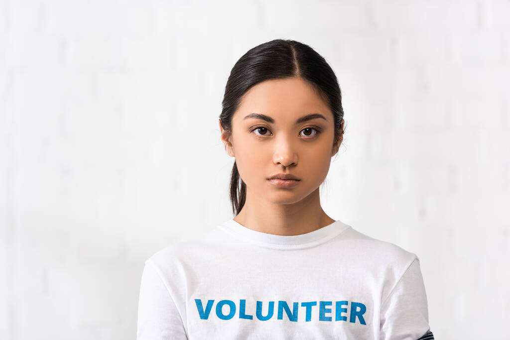チャリティセンターでカメラを見てボランティアレタリングTシャツを着たアジアの女性  - 写真・画像