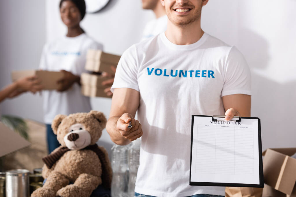 Enfoque selectivo del voluntario sujetando el portapapeles y la pluma en el centro de caridad  - Foto, Imagen