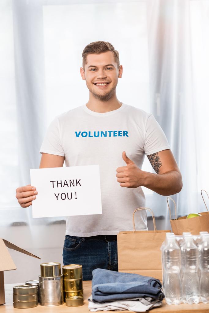 Önkéntes üdvözlőlap szelektív fókusza, köszönő betűkkel és az asztalon lévő konzervdobozok és papírzacskók közelében  - Fotó, kép