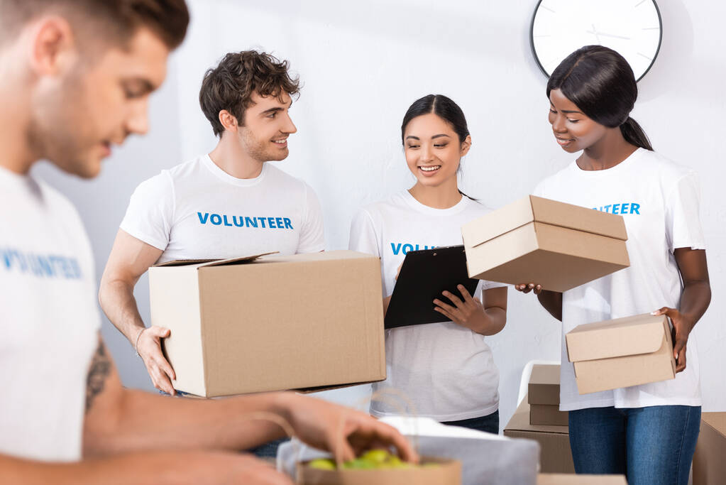 Selektivní zaměření multietnických dobrovolníků držících schránku a krabice v charitativním centru  - Fotografie, Obrázek