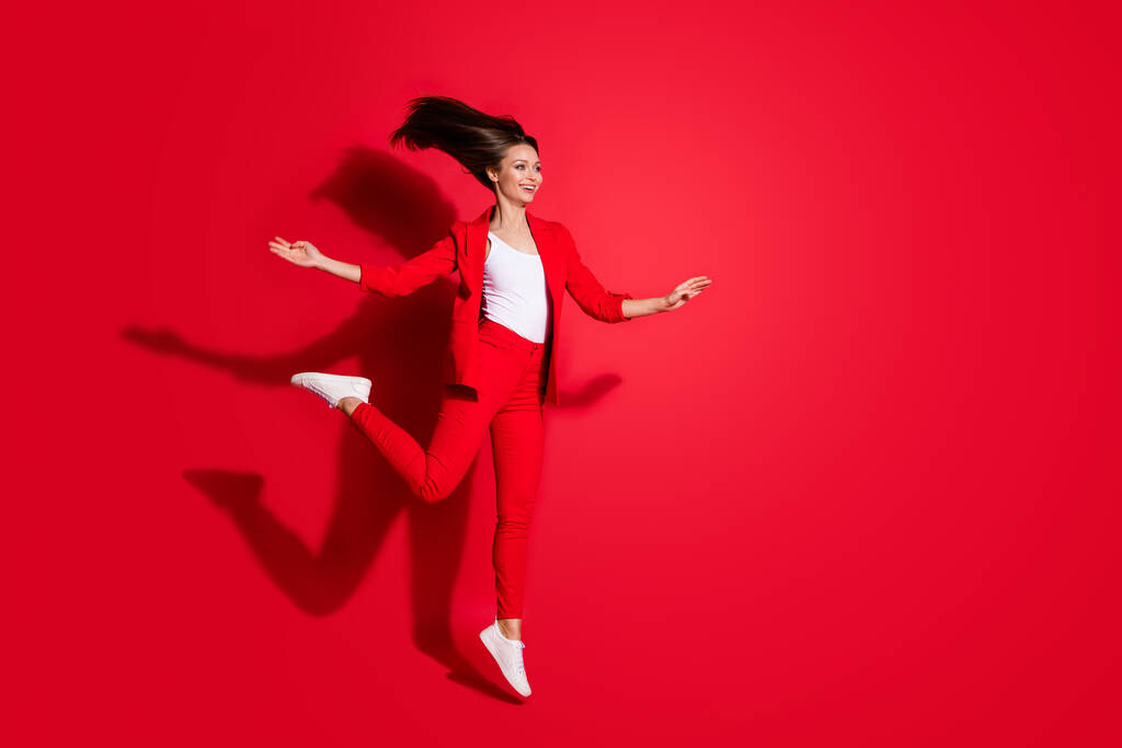 Volledige lengte profiel foto van aantrekkelijke werknemer dame die plezier springen hoog op goed humeur vakantie met plezier dragen blazer pak broek schoenen geïsoleerde helder levendige rode kleur achtergrond - Foto, afbeelding