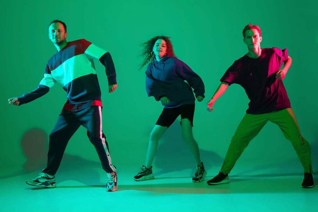 Hommes et femmes élégants dansant hip-hop en vêtements lumineux sur fond dégradé à la salle de danse dans la lumière au néon - Photo, image