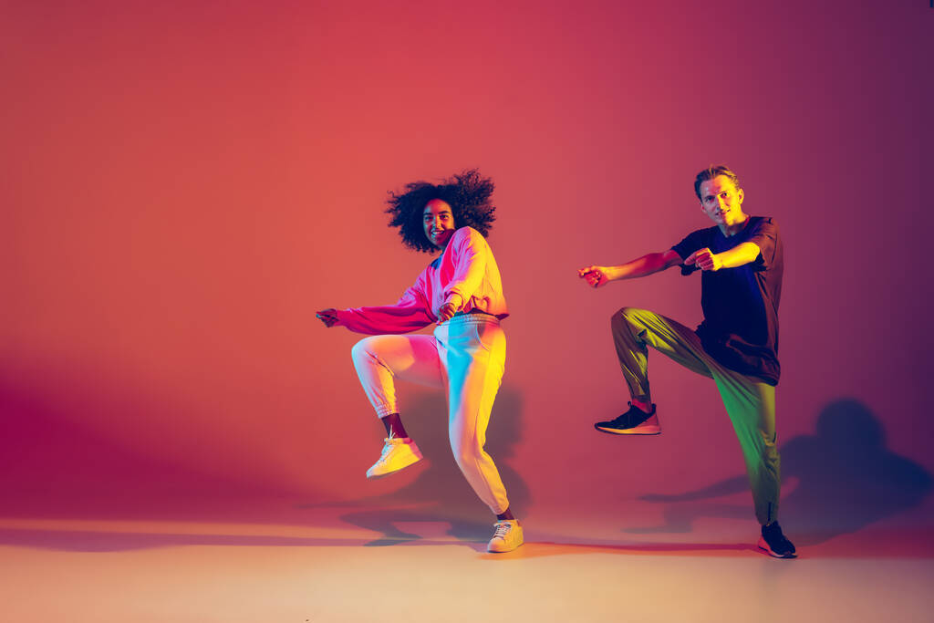 Hombre y mujer con estilo bailando hip-hop en ropa brillante sobre fondo degradado en la sala de baile en luz de neón - Foto, Imagen