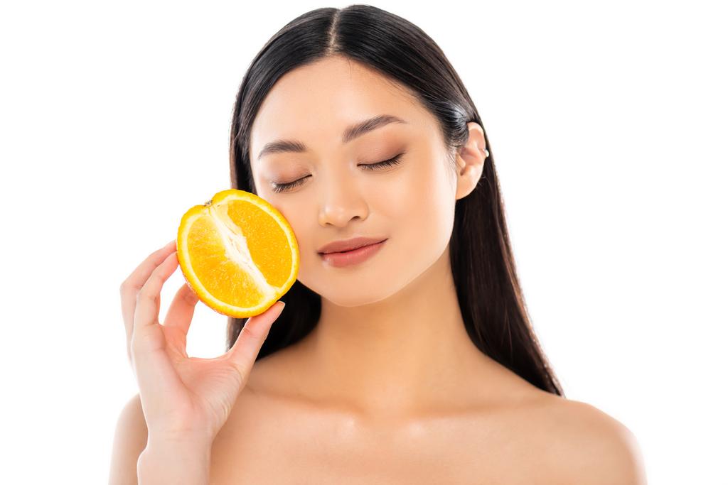 młoda Azjatka z zamkniętymi oczami trzymając połowę soczystej pomarańczy blisko twarzy odizolowany na białym - Zdjęcie, obraz