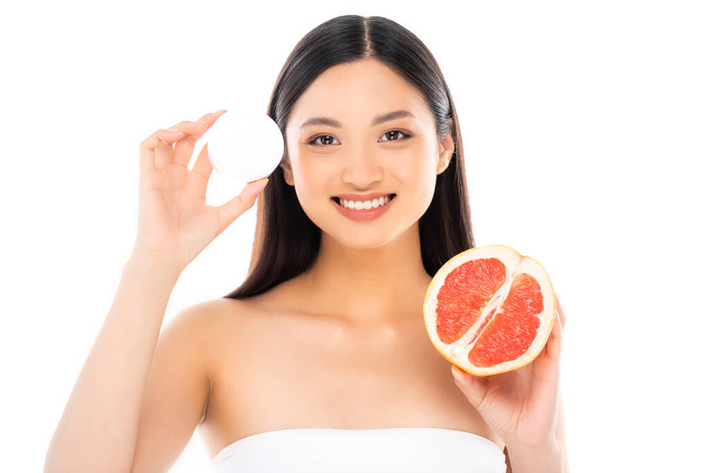 brunetka asijské žena při pohledu na kameru při držení poloviny šťavnaté grapefruit a kosmetické krém izolované na bílém - Fotografie, Obrázek
