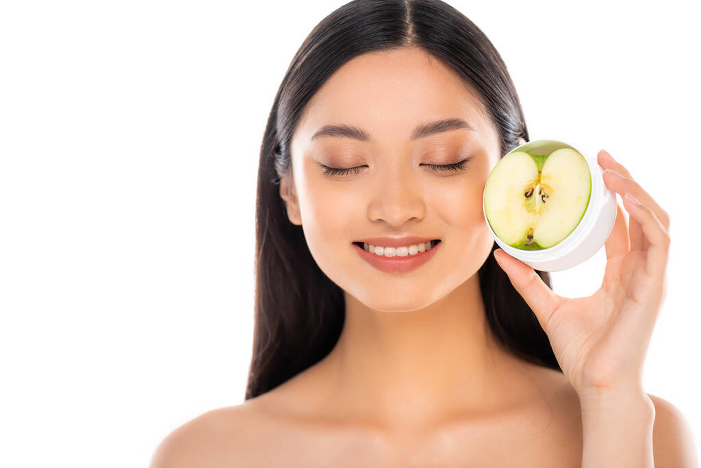 naakt aziatische vrouw met gesloten ogen houden helft van groene appel in de buurt gezicht geïsoleerd op wit - Foto, afbeelding