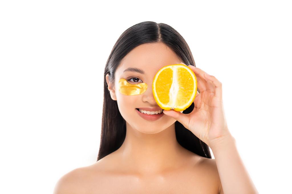брюнетка азиатская женщина с золотой косметический пластырь покрывающий глаз с половиной спелых оранжевый изолирован на белом - Фото, изображение