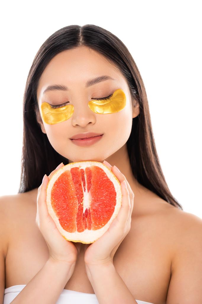 barna ázsiai nő arany szem foltok az arcon gazdaság fele érett grapefruit csukott szemmel elszigetelt fehér - Fotó, kép