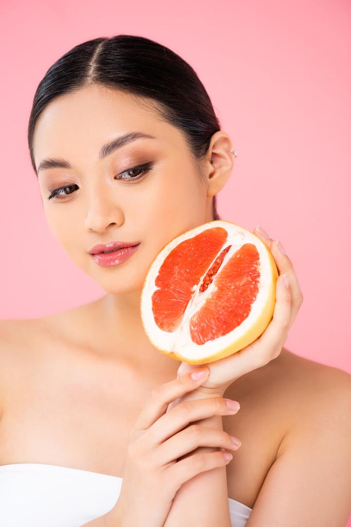 ázsiai nő gazdaság fél érett grapefruit közel arc elszigetelt rózsaszín - Fotó, kép