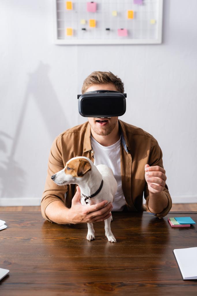 jonge zakenman in vr headset in de buurt van jack rassell terrier hond op het werk - Foto, afbeelding