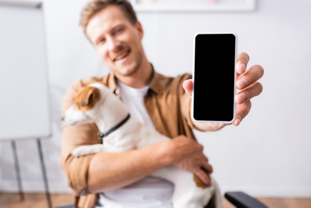 selektywne skupienie biznesmena pokazującego smartfona z pustym ekranem trzymając psa terrier jack russell - Zdjęcie, obraz