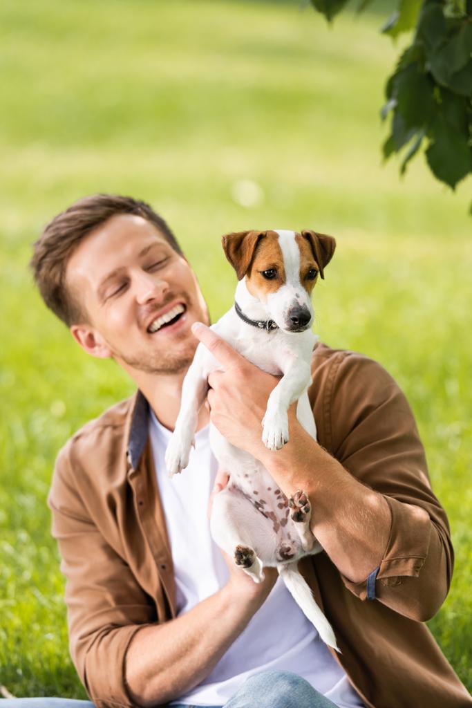 young man in brown shirt holding white jack russell terrier dog with spots on head - Photo, Image