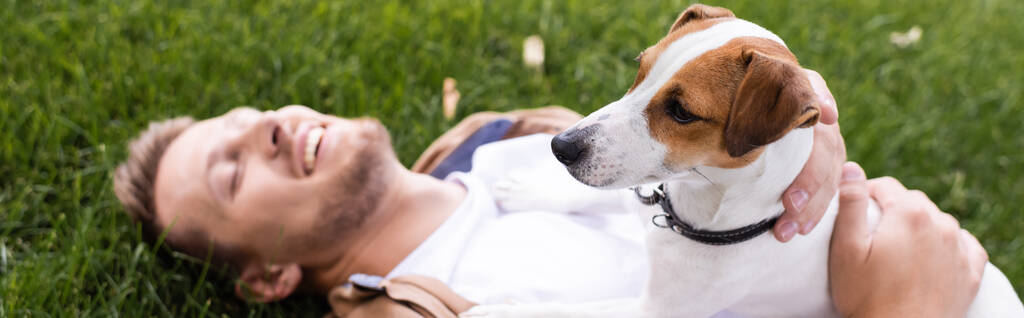 pozioma koncepcja człowieka leżącego na trawniku z zamkniętymi oczami i przytulającego psa terrier jack russell - Zdjęcie, obraz