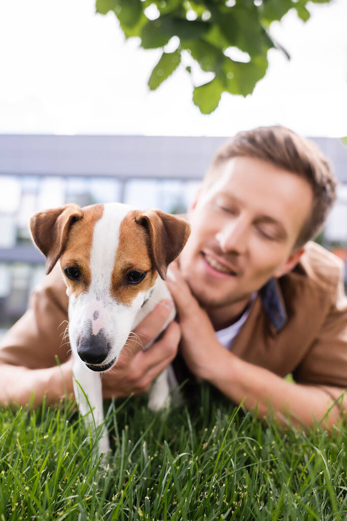 foyer sélectif de jeune homme couché sur l'herbe verte avec Jack Russell terrier chien - Photo, image