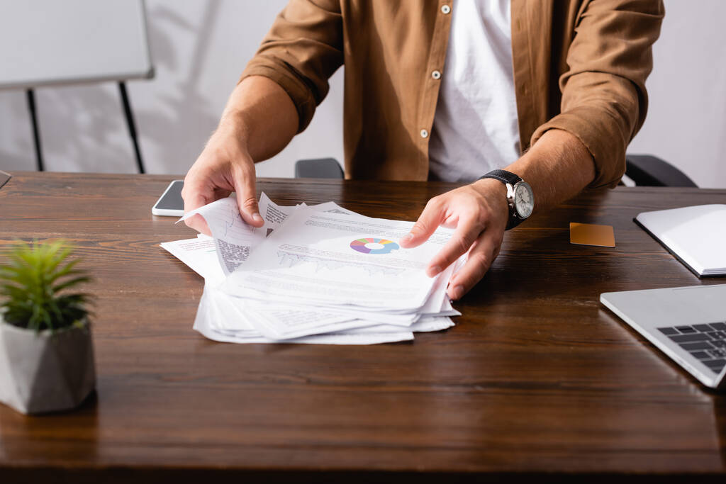 Обрізаний вид бізнесмена, який бере документи біля гаджетів на столі в офісі
  - Фото, зображення