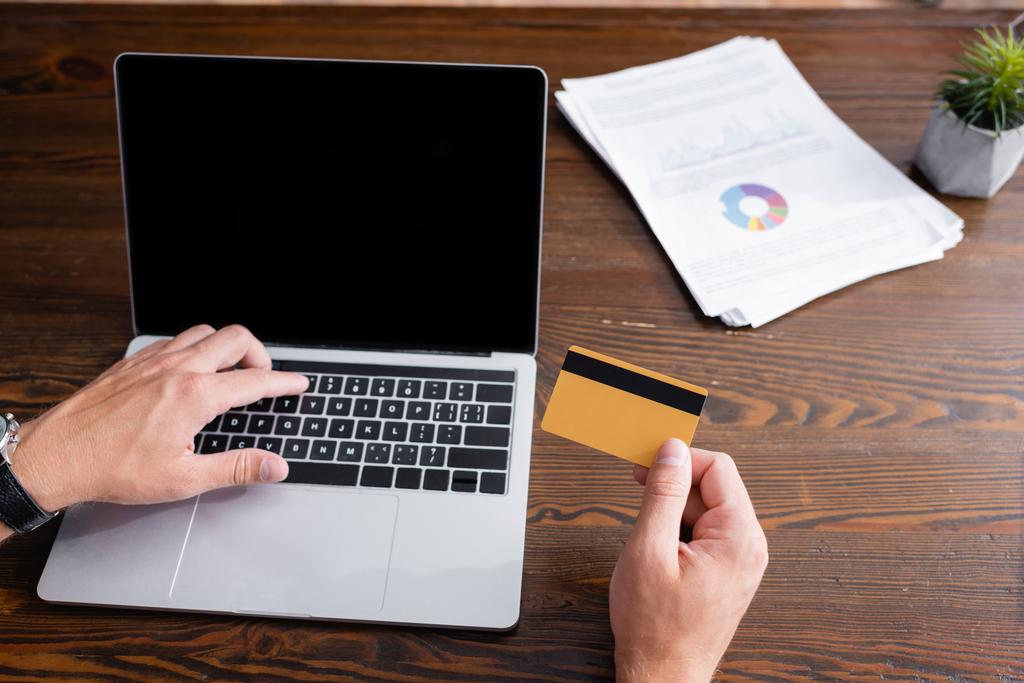 Oříznutý pohled na obchodníka držícího kreditní kartu a používajícího notebook s prázdnou obrazovkou v kanceláři  - Fotografie, Obrázek