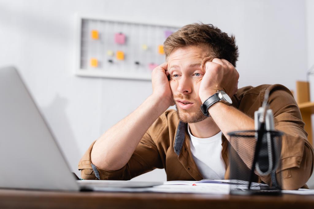 Επιλεκτική εστίαση του εξαντλημένου επιχειρηματία κοιτάζοντας φορητό υπολογιστή στο γραφείο   - Φωτογραφία, εικόνα