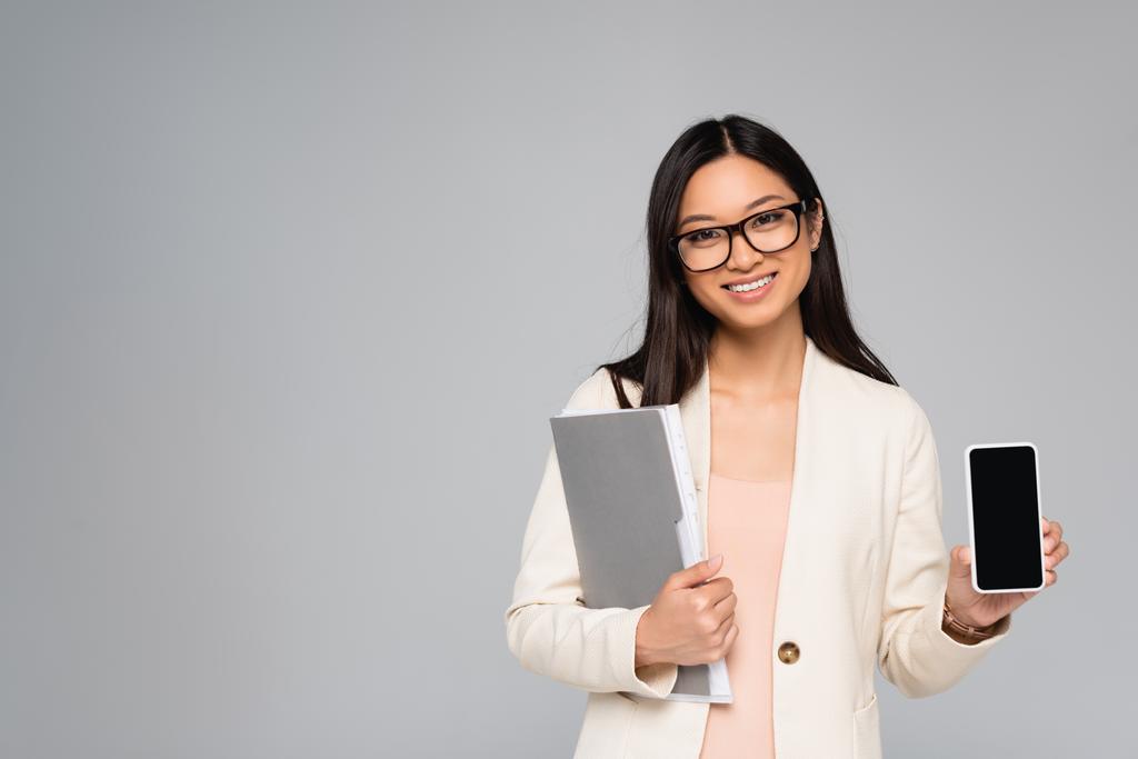 mujer de negocios asiática en gafas con carpeta y teléfono inteligente con pantalla en blanco aislado en gris - Foto, imagen