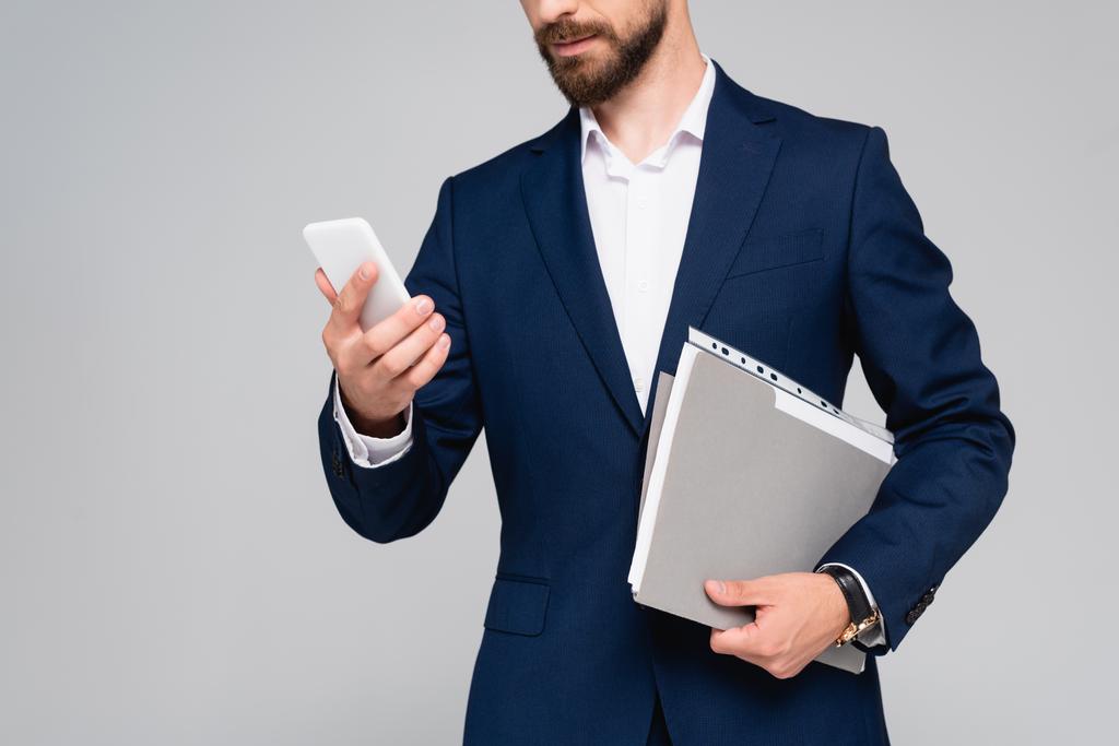 vista recortada del hombre de negocios en blazer azul con teléfono inteligente y documentos aislados en gris - Foto, Imagen