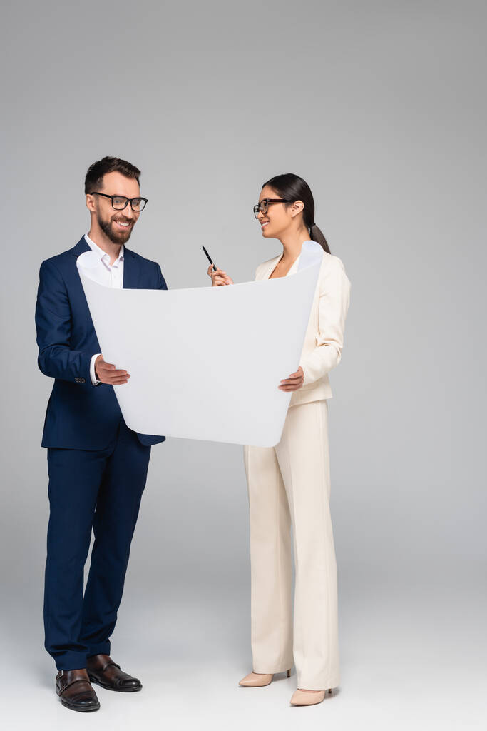 Ασιάτισσα επιχειρηματίας που μιλάει με επιχειρηματία ενώ κρατάει λευκή βίβλο στο γκρι - Φωτογραφία, εικόνα