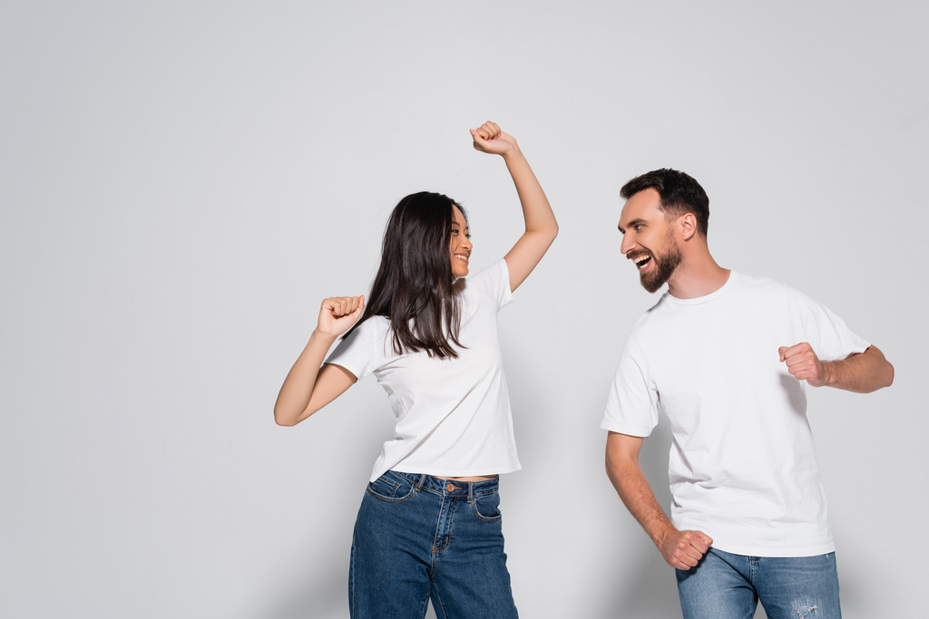 pareja interracial joven en camisetas blancas bailando mientras se miran en blanco - Foto, imagen