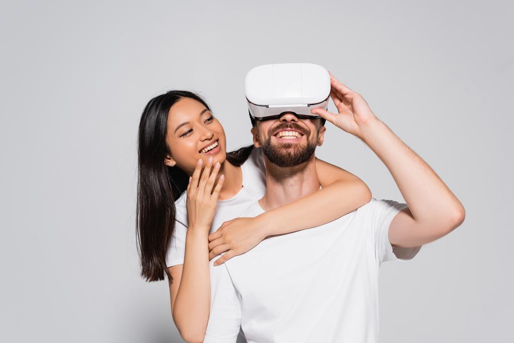 young asian woman hugging excited boyfriend gesturing in vr headset on grey - Photo, Image