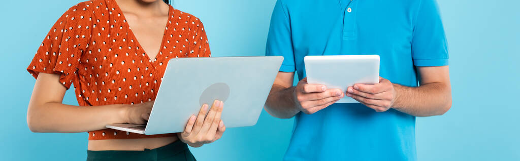 частковий вигляд жінки в червоній блузці з ноутбуком біля чоловіка з цифровим планшетом на синьому, горизонтальному посіві
 - Фото, зображення