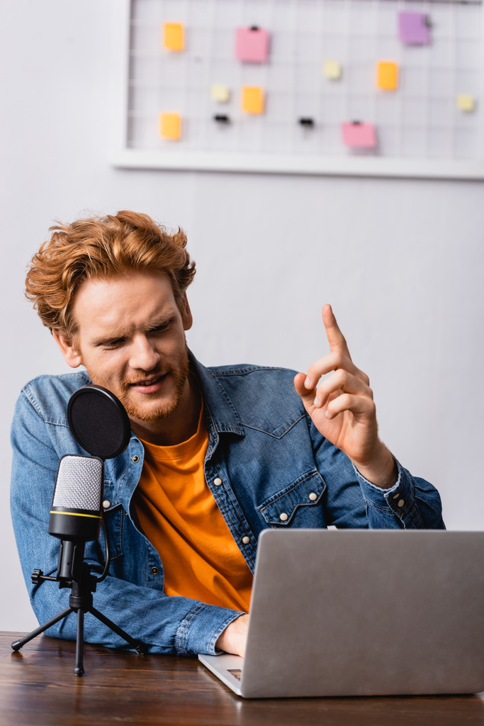 vörös hajú műsorszolgáltató farmer ing mutatja ötlet gesztus, miközben beszél mikrofonban közelében laptop - Fotó, kép