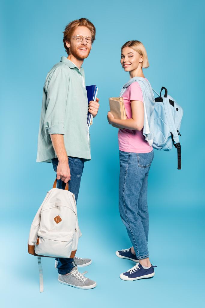 jonge studenten met rugzakken met notitieboekjes en boeken terwijl ze op blauw staan  - Foto, afbeelding