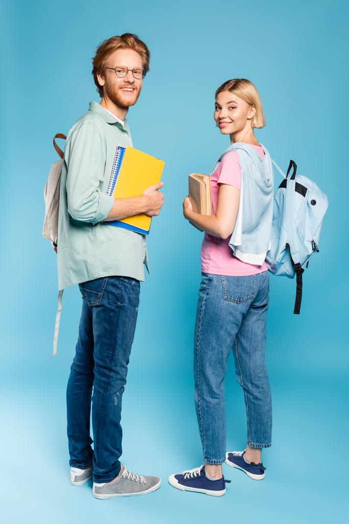 estudiantes con mochilas sosteniendo cuadernos y libros mientras están de pie en azul  - Foto, imagen