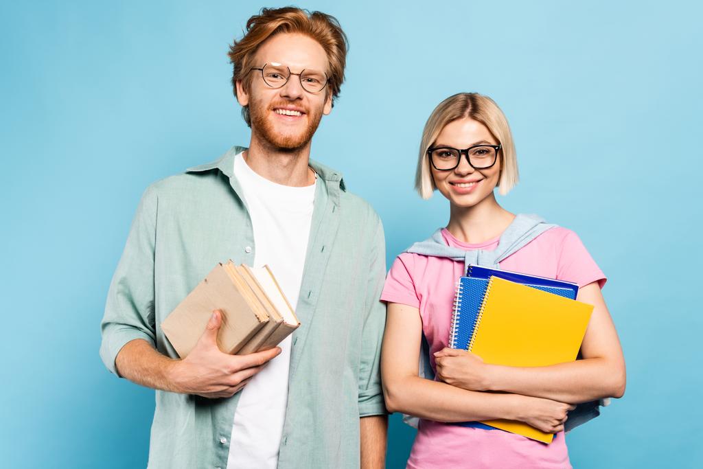 mladí studenti v brýlích drží zápisníky a knihy, zatímco stojí na modré  - Fotografie, Obrázek