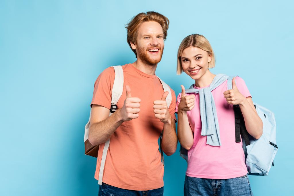 mladí studenti s batohy ukazující palce nahoru na modré - Fotografie, Obrázek