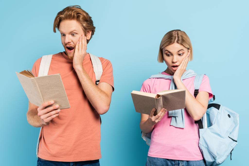 mladí šokovaní studenti čtení knih a dotýkání tváře na modré - Fotografie, Obrázek