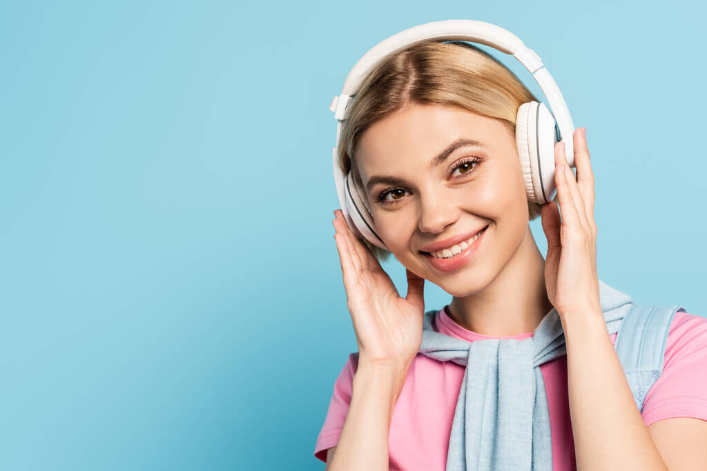 mujer rubia escuchando música en auriculares inalámbricos en azul - Foto, Imagen