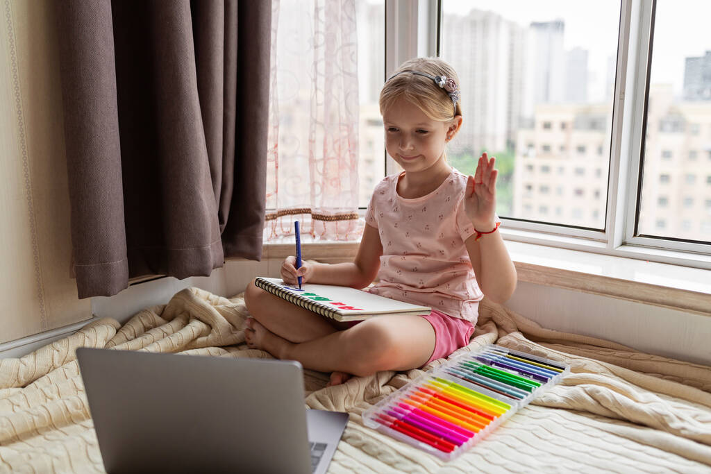 Kisgyerek angol online otthon. Otthoni oktatás és távoktatás gyerekeknek. Egy lány, aki angol betűket rajzol a füzetbe a koronavírus kovid-19 karantén alatt. Kiváló minőségű fénykép - Fotó, kép