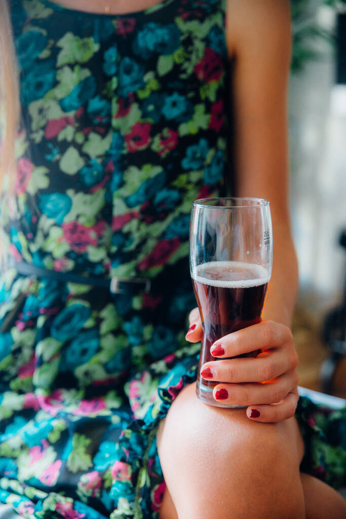 Ein sanfter Fokus einer Frau in buntem Kleid, die ein Glas Getränk auf ihrem Schoß hält - Foto, Bild
