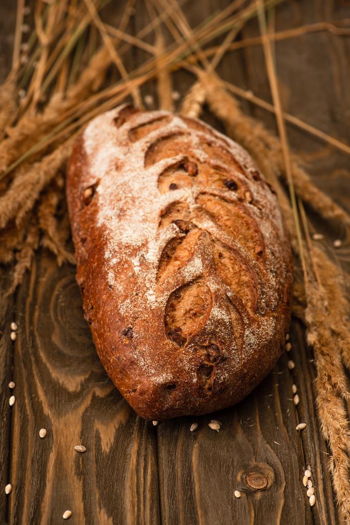 selectieve focus van vers gebakken brood brood met spikeletten op houten oppervlak - Foto, afbeelding