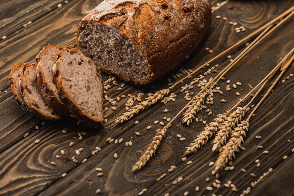 cut fresh baked bread with spikelets on wooden surface - Photo, Image
