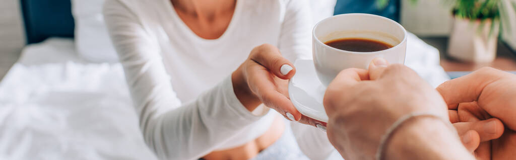 colheita horizontal de homem dando xícara de café para namorada no quarto - Foto, Imagem