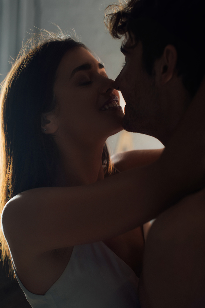 Молодая женщина целует парня без рубашки вечером дома  - Фото, изображение