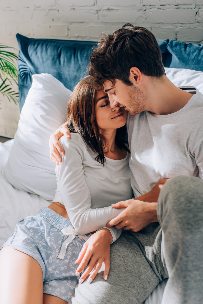 朝の間にベッドにしがみつくパジャマで若いカップルの選択的な焦点  - 写真・画像