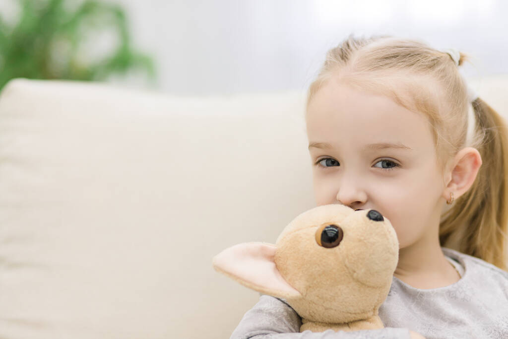 Portrait of adorable blonde girl lying on sofa holding toy in her arms on white background. - 写真・画像