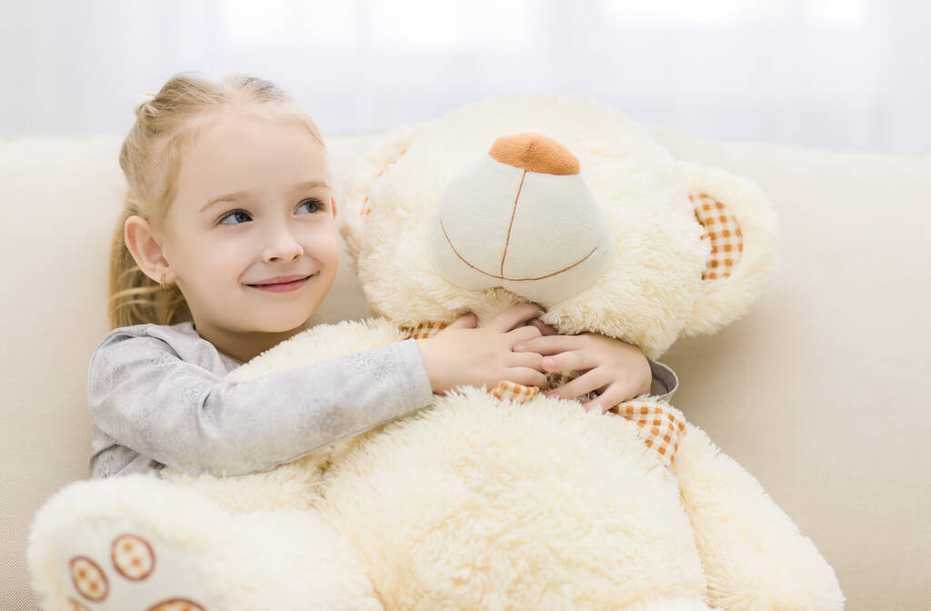 Маленька дівчинка обіймає великого плюшевого ведмедя
. - Фото, зображення