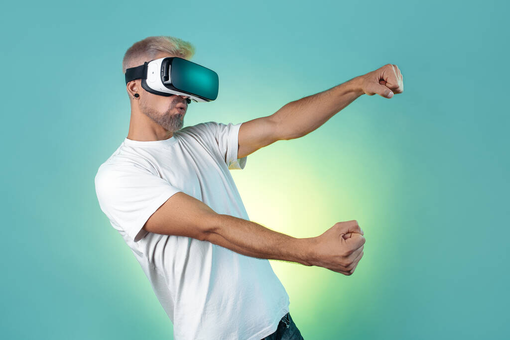 Gladful barbudo hipster hombre con pelo rubio con gafas de realidad virtual en el estudio en luces de neón. - Foto, Imagen