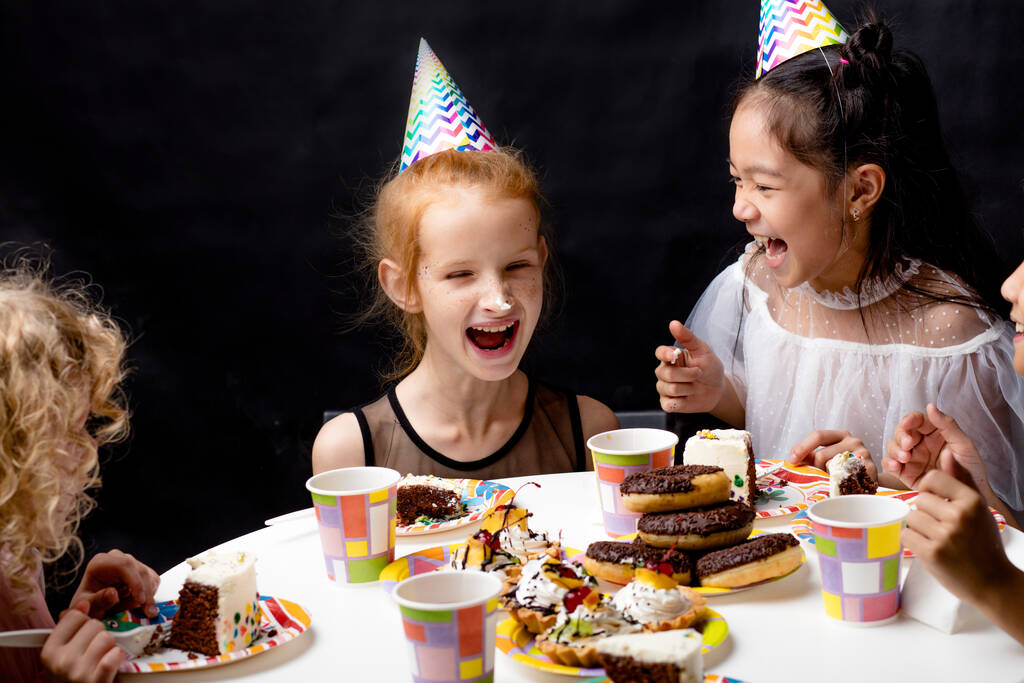 Κορίτσια με τούρτα στη μύτη γελάνε ενώ κάθονται στο τραπέζι. - Φωτογραφία, εικόνα