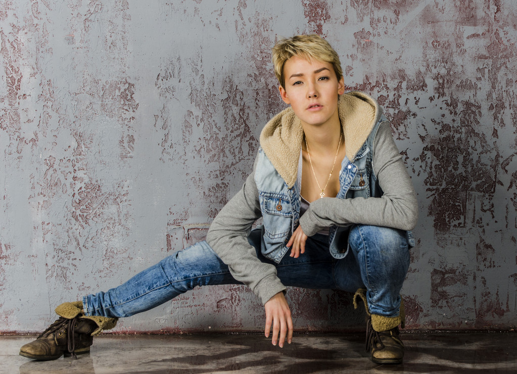 Jeune belle fille aux cheveux courts en jeans et une veste en denim assise au mur en bois
 - Photo, image