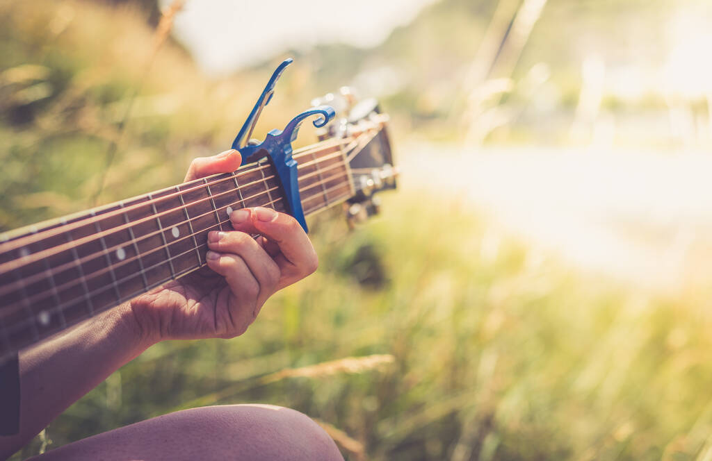 Nahaufnahme einer Westerngitarre, die im Sommer draußen an einem Fluss gespielt wird - Foto, Bild