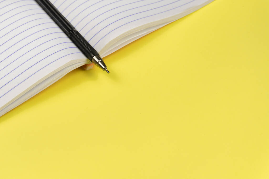 A set of office supplies. Blank notepad and pen isolated on bright yellow background. - Photo, Image