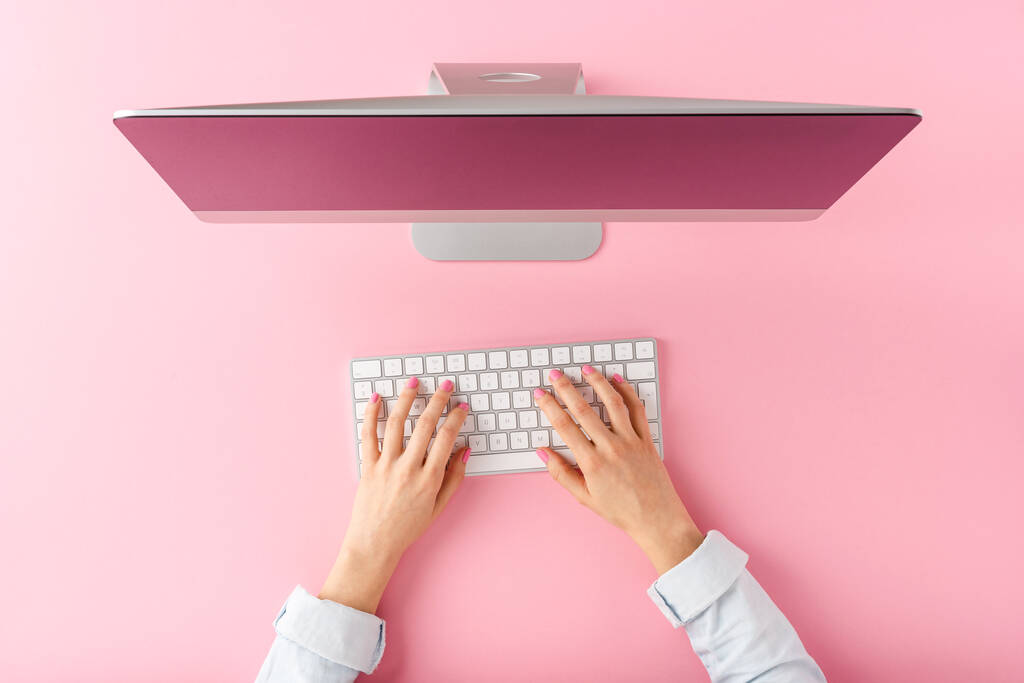 Концепция рабочего стола. Женские руки работают на компьютере на розовом фоне. Вид сверху - Фото, изображение
