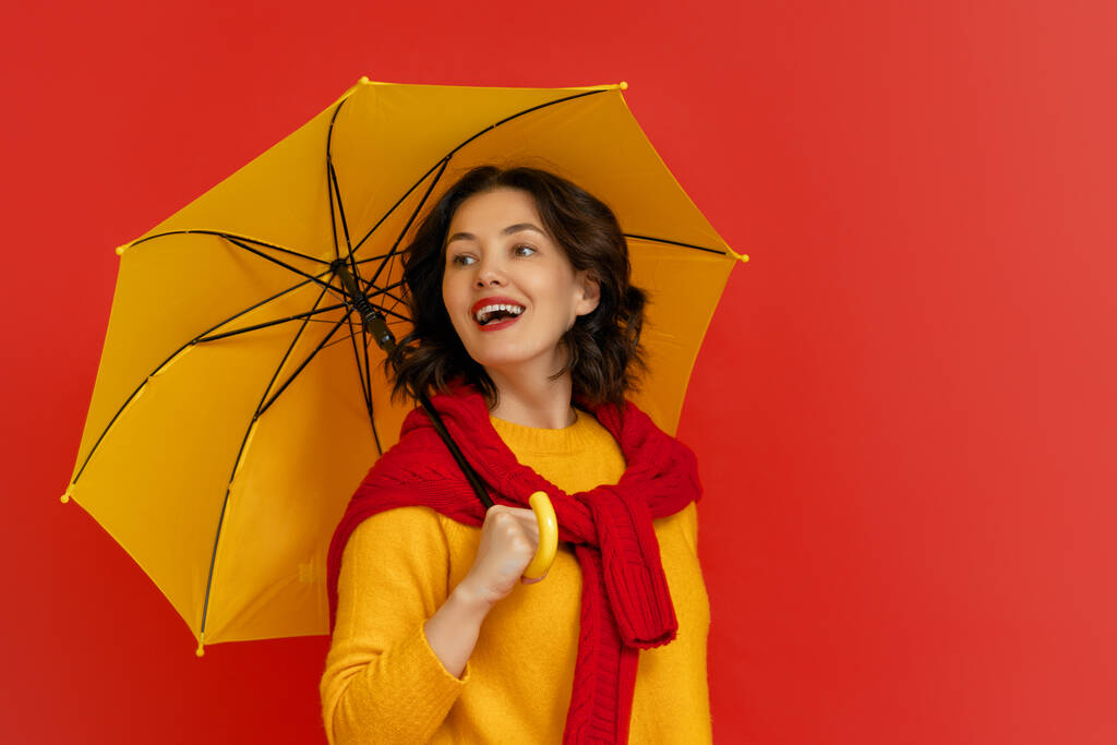 Happy emotional young woman laughing with yellow umbrella on color red background. - Photo, Image